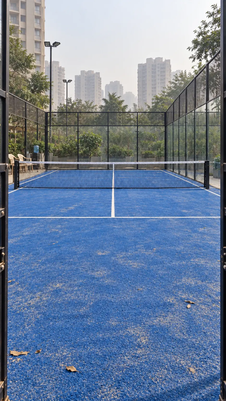 An empty padel court on a quiet morning, tower blocks behind it